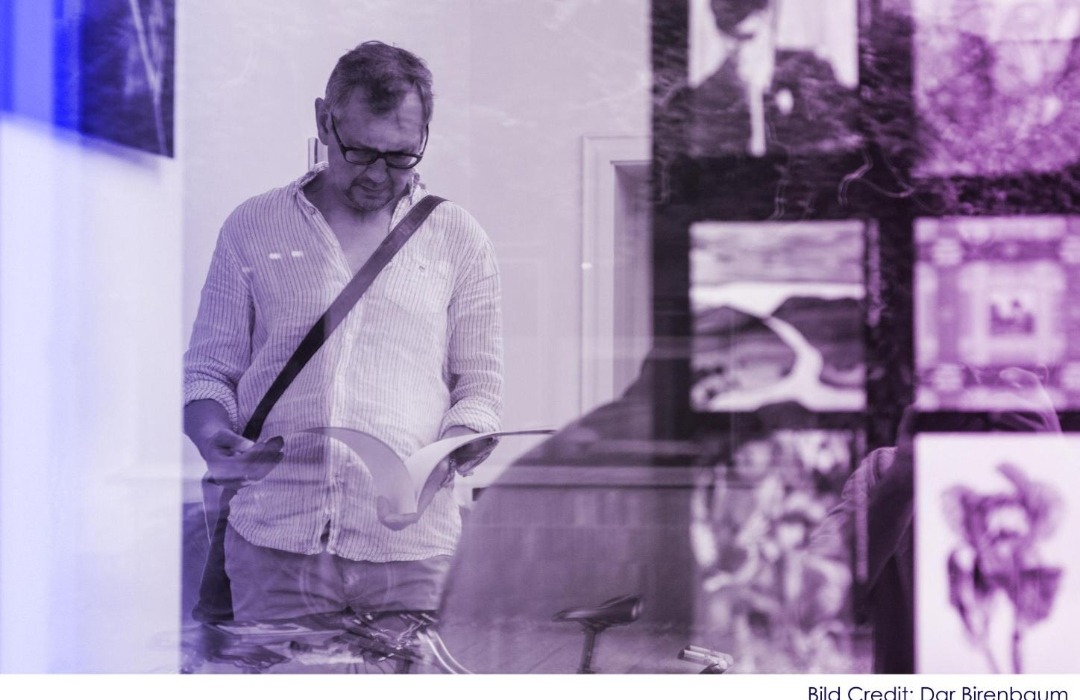 Besucher betrachtet Kunstwerke in der Galerie 20blue.arts durch eine Glasscheibe mit Reflexionen