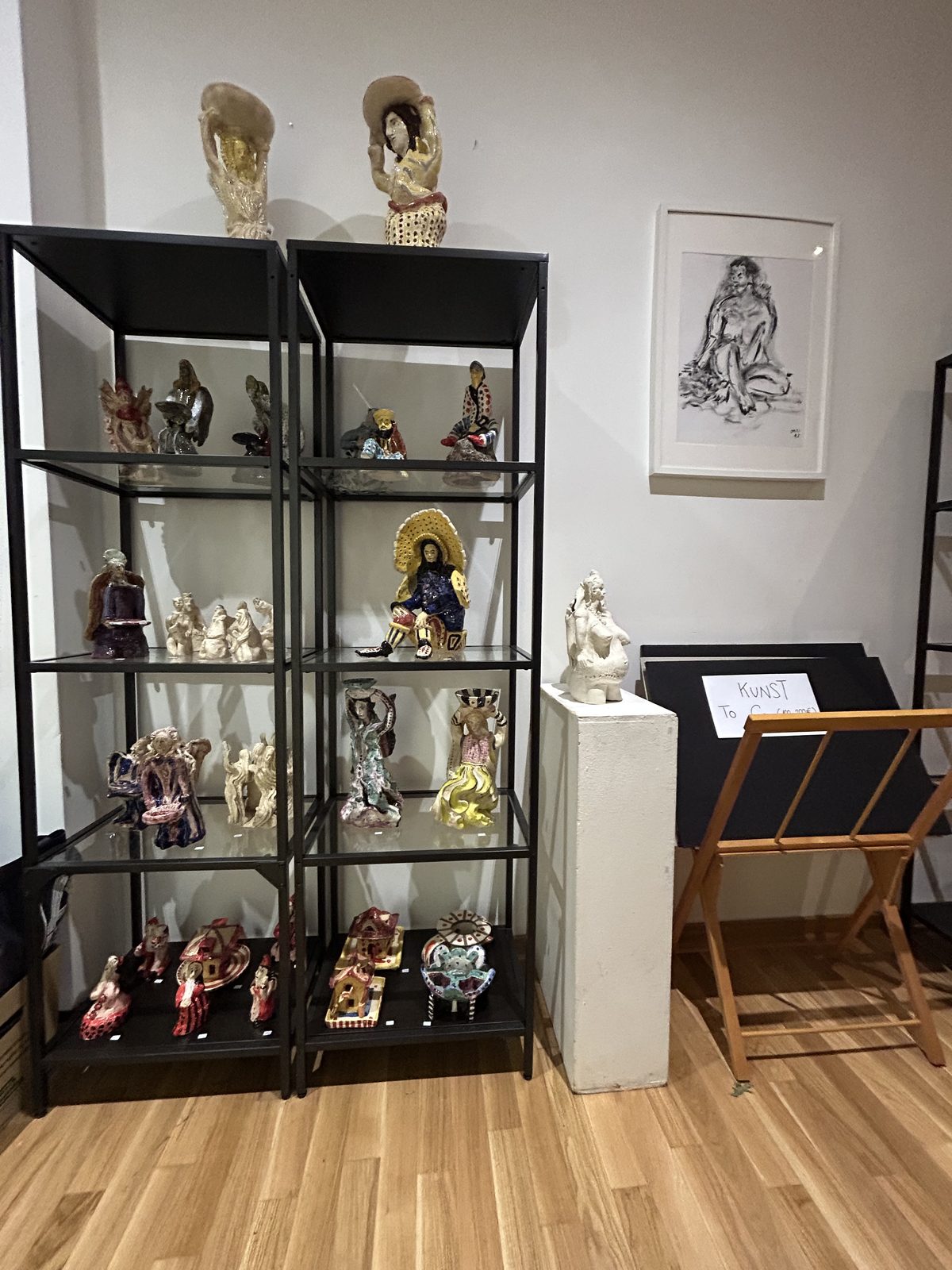 Regal mit Keramikfiguren, Engeln und Kunstobjekten in der Galerie 20blue.arts, daneben eine gerahmte Zeichnung